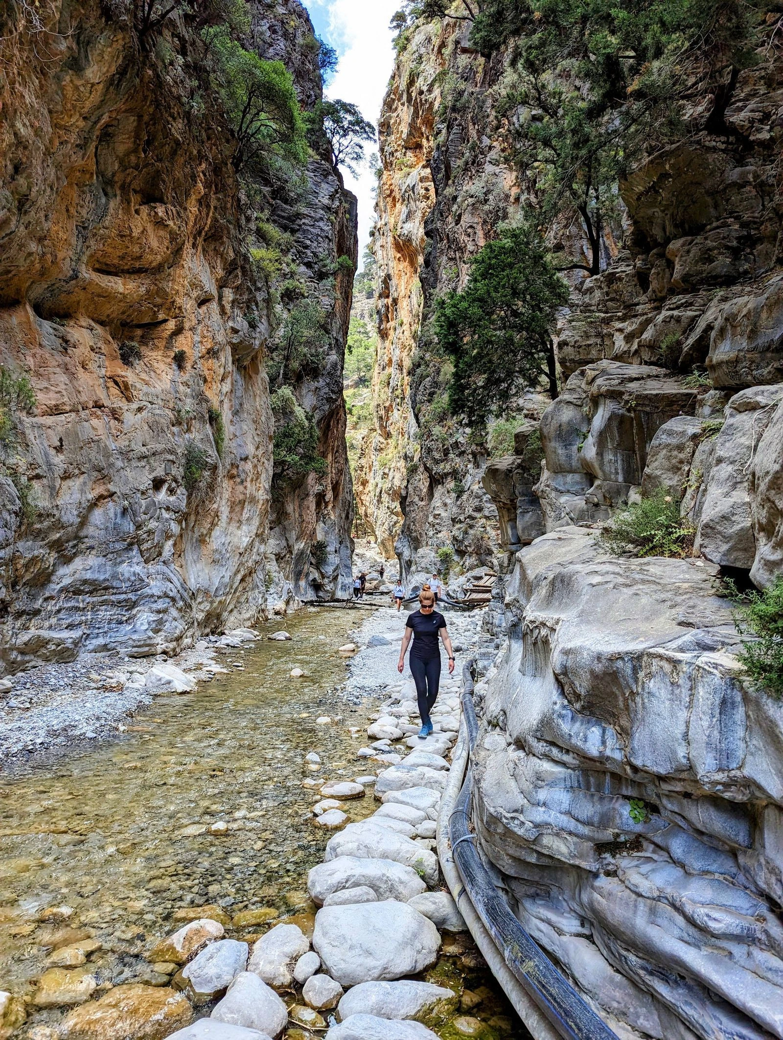 Hikers walking along the narrow stone path inside the dramatic rock walls of Samaria Gorge